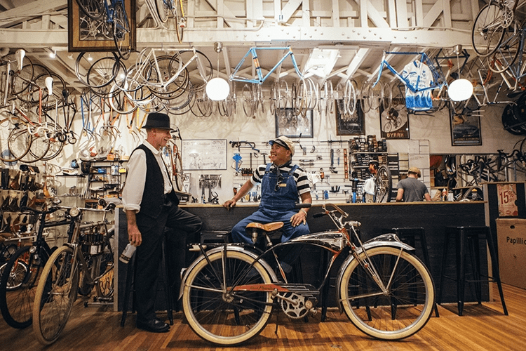 two mens sitting on a bicycle in a bicycle shop